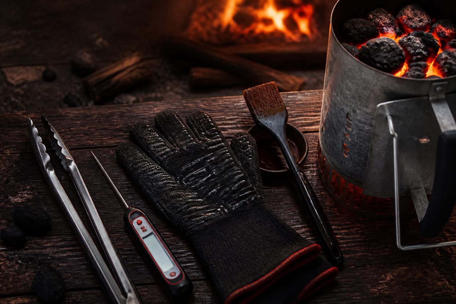 Ensemble d'accessoires de barbecue posés sur une table : thermomètre à sonde, pince, gants et cheminée d'allumage