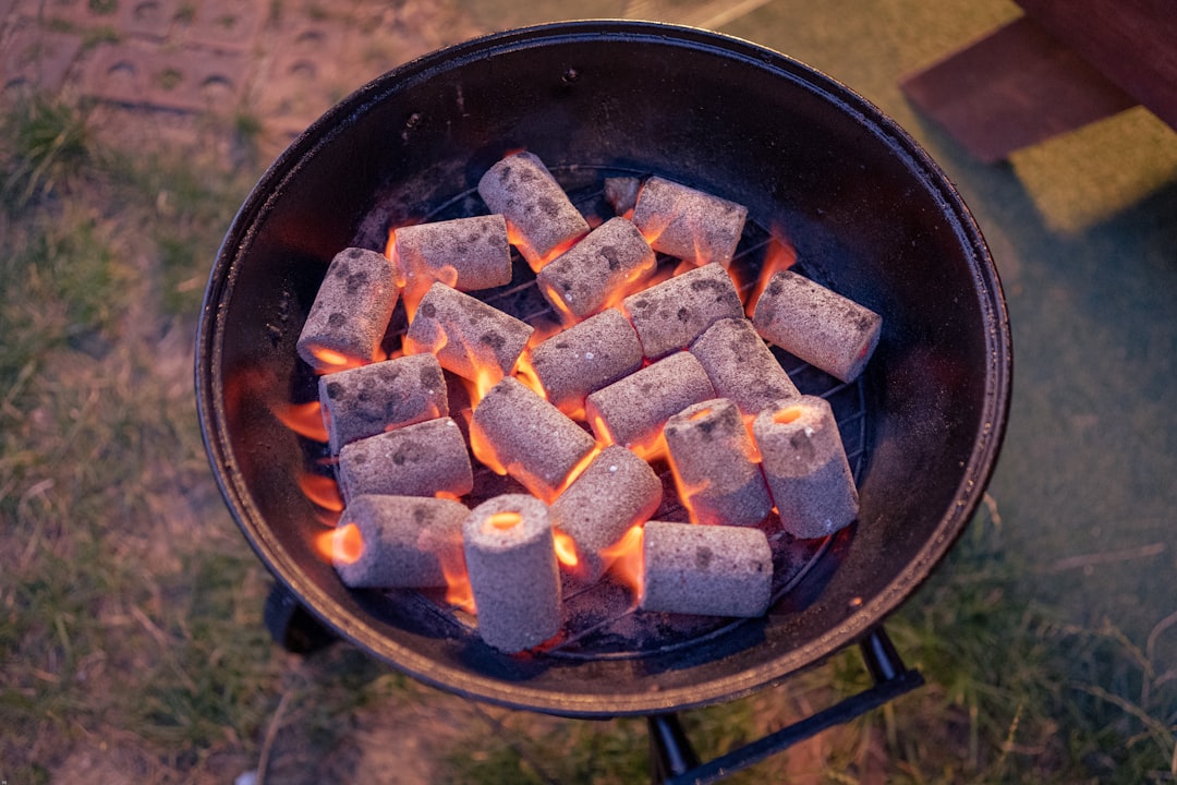 Barbecue à charbon d’entrée de gamme installé dans un jardin, couvercle ouvert et braises allumées.