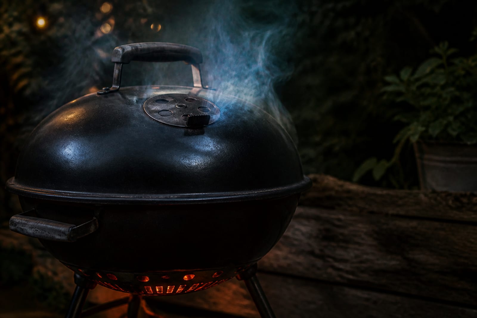 Fine fumée bleutée s'échappant d'un barbecue à couvercle fermé au crépuscule, braises rougeoyantes visibles par la grille d'aération