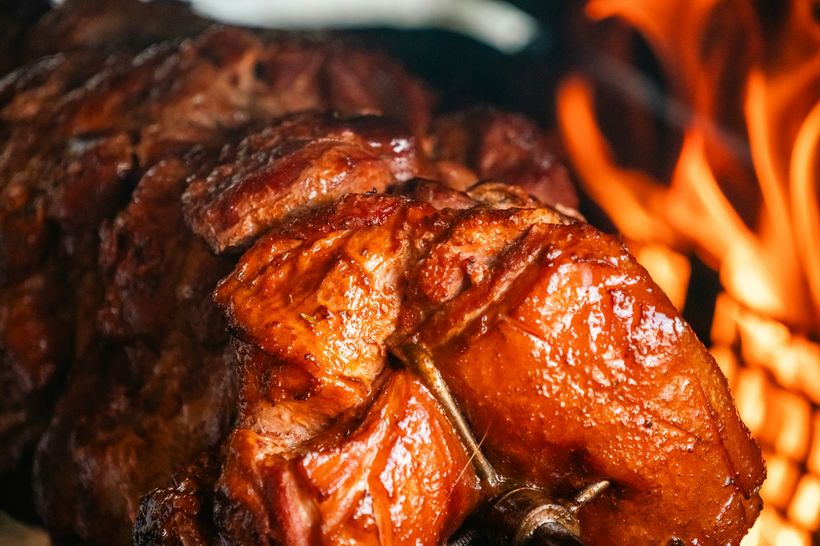 Pièce de poitrine de porc laquée et brillante en cuisson sur la grille d'un barbecue, flammes visibles dessous