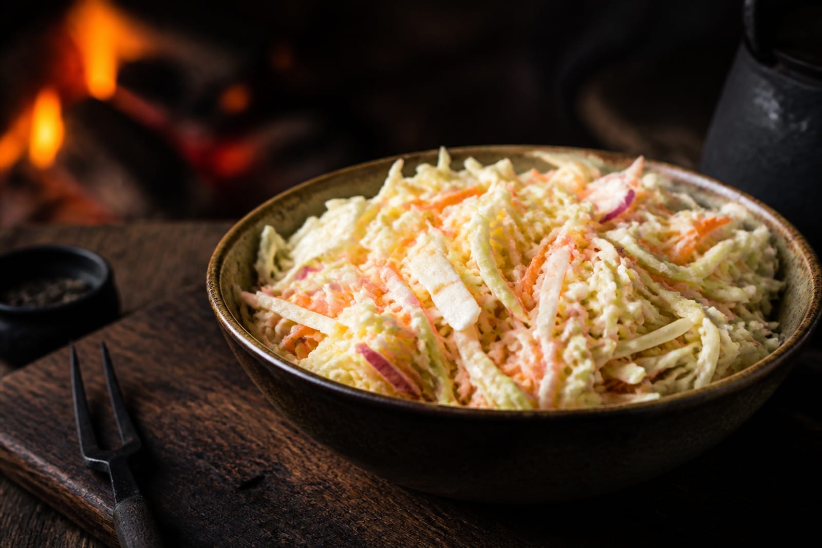 Coleslaw crémeux de chou blanc et carotte râpée finement émincés dans un bol, frais et croquant, sur une planche en bois sombre